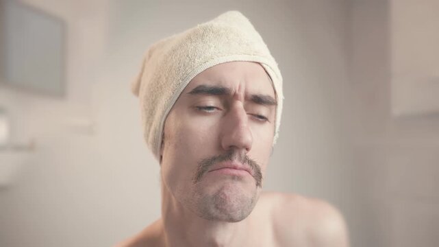 Comical mustached man in bathroom with towel on head making stop hand gesture and showing discontent and contemplation
