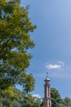 Vertical minimalist background featuring a mosque minaret and vibrant green foliage under a sunny sky. High-quality stock photo with large negative space for text layout, posters, or social media stor