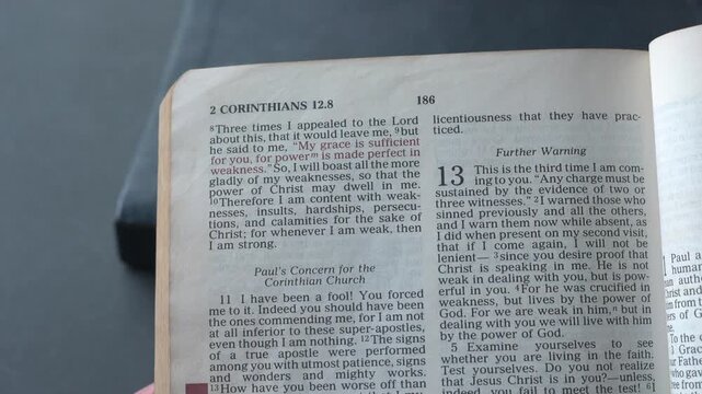Holy Bible open up to the book of 2 Corinthians of the new testament, zooming into Chapter 12 verse 9 on God&rsquo;s grace sufficiency. New Revised Standard Version