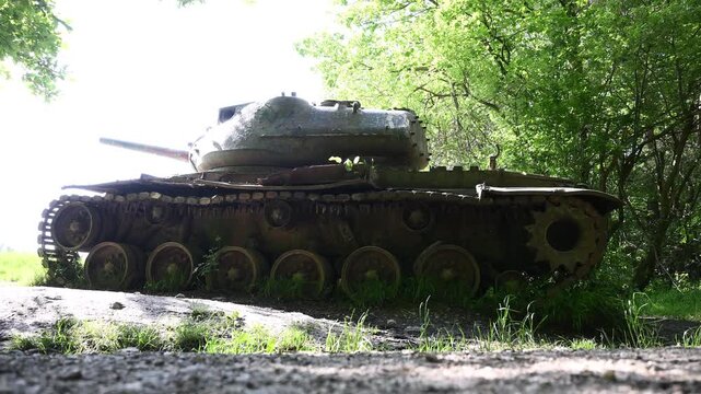 An abandoned, rusted tank stands in a forested area as a historic military object.