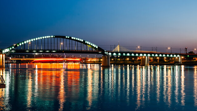 View of the Old Sava Bridge illuminated with green lights over the Sava River at dusk with reflections in the water Belgrade, City of Belgrade, Serbia.