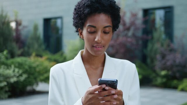 Gadget addict African American business woman using mobile phone app outdoors ethnic girl female browsing smartphone in city businesswoman student manager scrolling social media online device outside