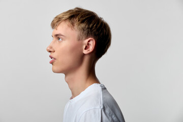 Obraz premium Profile of a young man in a plain white tee, side view against a neutral backdrop, calm expression and clean studio lighting for a minimalist, versatile image