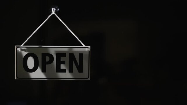 Hand flipping 'open' sign to 'closed' on dark background, business closed sign, end of day.