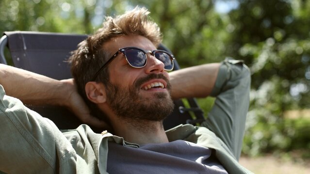 A man is relaxing in a chair with his arms around his neck
