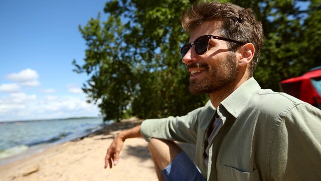 A man is sitting on the beach wearing sunglasses and a green shirt