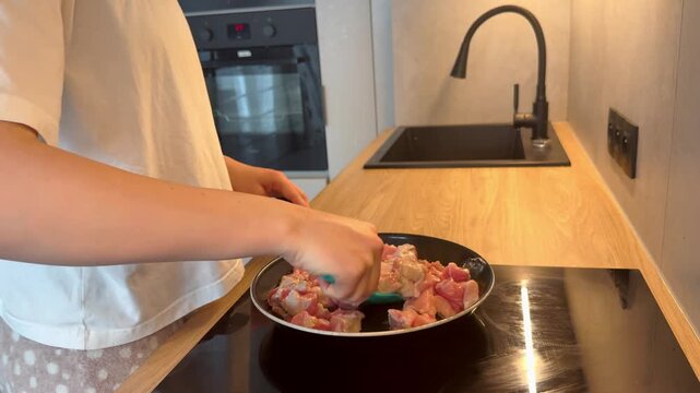 Hand stirring diced pork and beef in a hot non-stick frying pan on an induction cooktop. Modern kitchen cooking scene showcasing sizzling meat, culinary technique, and meal preparation 