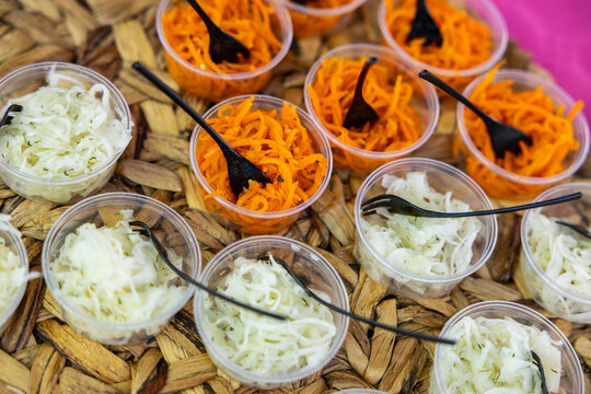 Plastic cups of shredded carrot and cabbage salad with black forks on a woven tray, framed by gray copy space