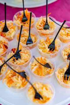 Clear plastic cups filled with shredded cabbage and carrot salad, each served with black forks on a white tray