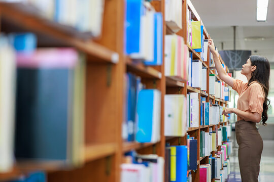 A dedicated female university student reviews academic literature and course materials in a campus library. A concept of higher education, scholarships, and academic success.