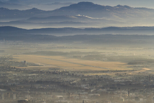 View of the Graz Airport runway and city skyline nestled among misty hills and rolling mountains under a hazy sky Graz, Styria, Austria.