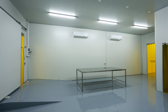 Empty sterile cleanroom laboratory features central metal table surrounded by white wall surfaces creating cold clinical calm atmosphere for research