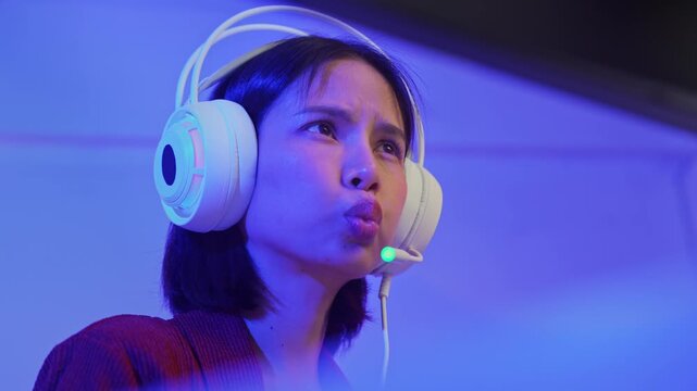Excited young Asian girl playing online computer game with headset and microphone at home, esports and live streaming concept.