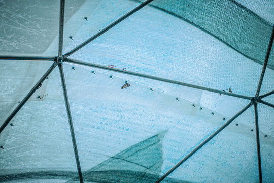 Geometric structure of a translucent dome with metal framework and blue sky visible through the mesh fabric.