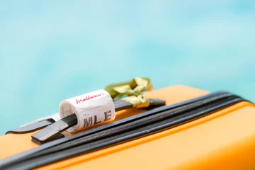 02.05.25, Male, Maldives - Bright orange suitcase with sign for "Maldives" is visible, suggesting a tropical vacation, blue background, relaxation. , travel, escape, leisure, beach. Summer holiday. © FOTO_STOCKER