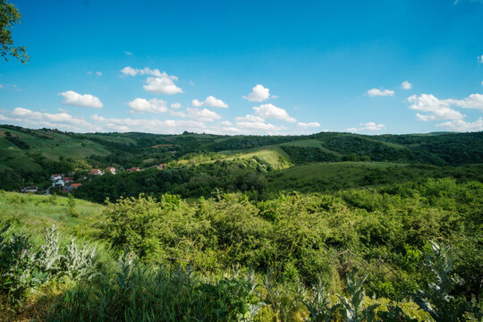 View of rolling green hills and a small village nestled in the valley under a blue sky with scattered clouds Bukovac, Vojvodina, Serbia.