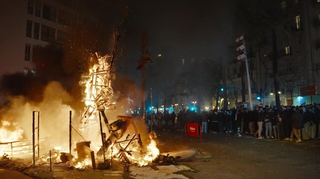 VALENCIA, SPAIN - MARCH 19, 2026: A burning falla structure sends a shower of sparks into the air during Las Fallas La Crema in Valencia, a crowd behind barriers watching, slow motion
