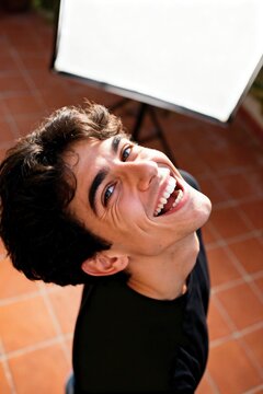 Joyful young Italian man laughing and looking up at the camera in energetic high angle top down portrait.