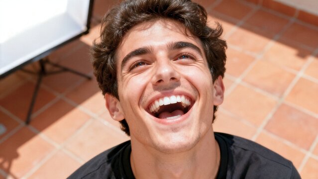 Joyful young Italian man laughing and looking up at the camera in energetic high angle top down portrait.