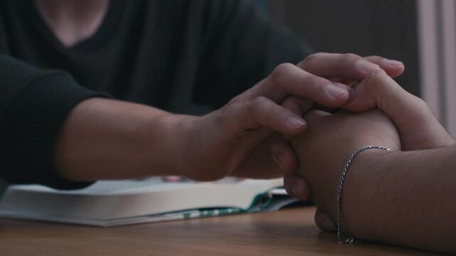 Close-up of a person praying with hands over an open book on a wooden table, spiritual reflection, faith, worship, and quiet devotion indoors