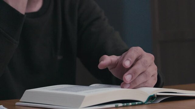 Close-up of a person praying with hands over an open book on a wooden table, spiritual reflection, faith, worship, and quiet devotion indoors