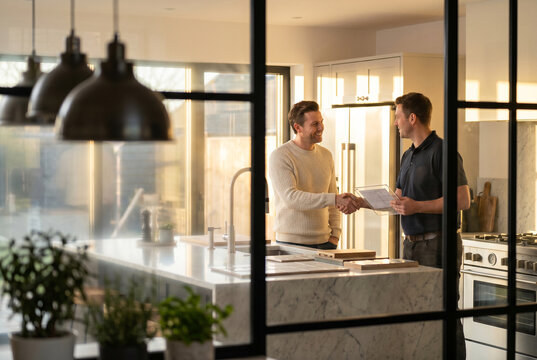 Homeowner shaking hands with contractor in luxury modern kitchen, home renovation consultation, remodeling project, interior design planning, residential construction, premium real estate lifestyle