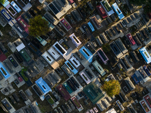 Aerial view of the colorful graves and headstones at Sasana Laya Gipik Plaosan cemetery with scattered trees in Kecamatan Prambanan, Jawa Tengah, Indonesia.