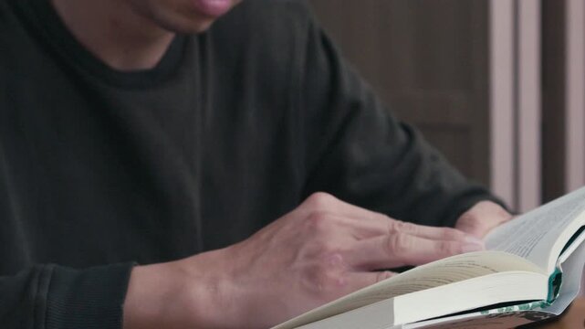 Close-up of a person praying with hands over an open book on a wooden table, spiritual reflection, faith, worship, and quiet devotion indoors
