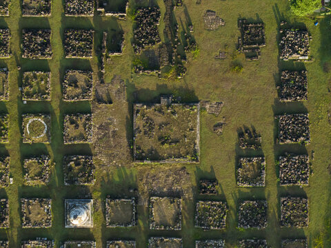 Aerial view of the ancient stone foundations and square ruins of Plaosan Kidul Temple on a green grassy field in Kecamatan Prambanan, Jawa Tengah, Indonesia.