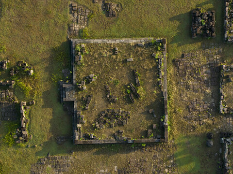 Aerial view of the ancient stone foundations and ruins of Plaosan Kidul Temple surrounded by green grass in Kecamatan Prambanan, Jawa Tengah, Indonesia.