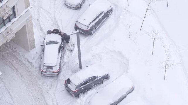 People pushing a stranded car through deep snow on a city street during heavy winter snowfall and difficult driving conditions