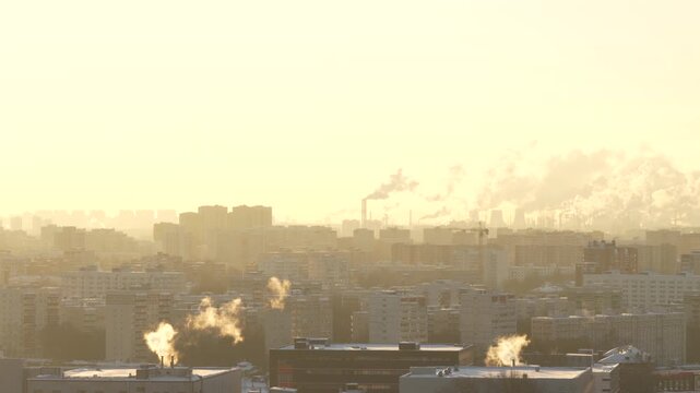 Panoramic urban skyline with residential buildings steam plumes and industrial chimneys in golden sunset light