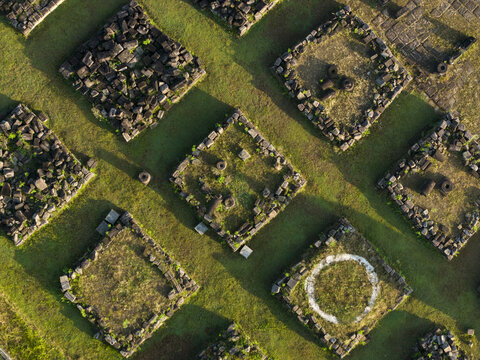 Aerial view of Plaosan Kidul Temple ruins with stone foundations and long shadows on green grass in Kecamatan Prambanan, Jawa Tengah, Indonesia.