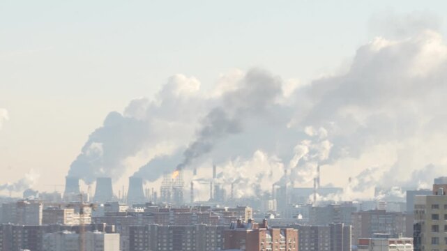 Industrial chimneys emitting smoke and steam over a densely populated urban area under cloudy sky