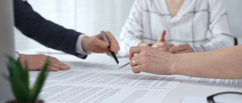 Business professionals reviewing contracts and paperwork in a meeting, pointing to key legal terms, negotiating and preparing signatures to finalize a collaborative agreement