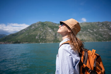 Profile portrait of a female traveler with an orange backpack looking at a scenic mountain lake. © olezzo