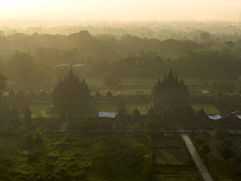 Aerial view of the ancient Plaosan Lor Temple complex shrouded in morning mist and surrounded by lush tropical greenery in Kecamatan Prambanan, Jawa Tengah, Indonesia.