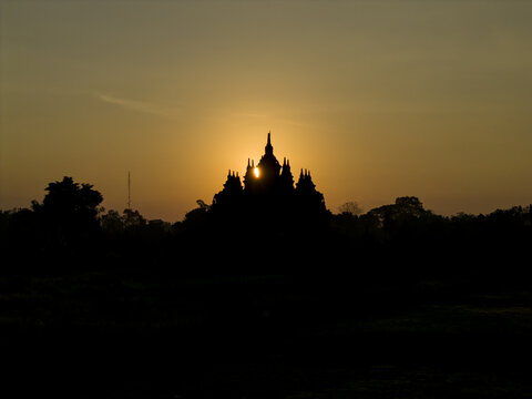 Aerial view of the silhouette of Plaosan Lor Temple during a golden sunset with the sun glowing behind the ancient stone spires Kecamatan Prambanan, Jawa Tengah, Indonesia.
