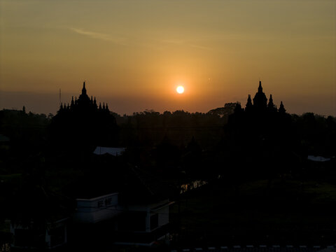 Aerial view of Plaosan Lor Temple silhouetted against a golden sunset sky with surrounding trees and fields Kecamatan Prambanan, Jawa Tengah, Indonesia.