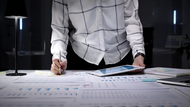 Business professional analyzing corporate financial data using digital tablet and documents, managing workload in late office hours, planning investment strategy and market growth