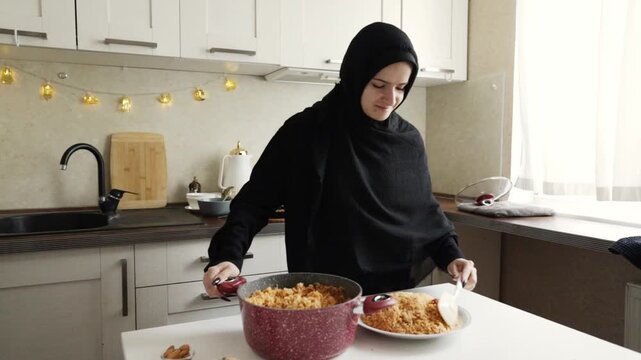 muslim woman in black hijab smiles as she shapes and plates a mound of seasoned rice from a deep red pot, preparing a celebratory homemade dish for a special gathering