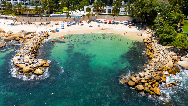 Aerial view of Playa Esmeralda featuring a turquoise water cove with people swimming and a rocky breakwater in Puerto Vallarta, Jalisco, Mexico.