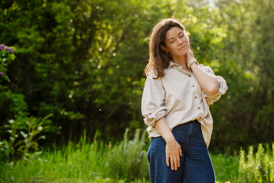 Happy mature woman enjoying nature and warm sunlight on her face in the green summer garden with backlighting.