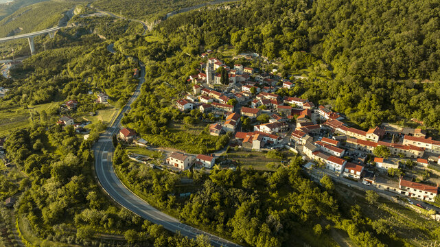 Aerial view of the historic village of Crni Kal with its red-roofed houses and church tower nestled among lush green hills and the viaduct in Crni Kal, Koper, Slovenia.