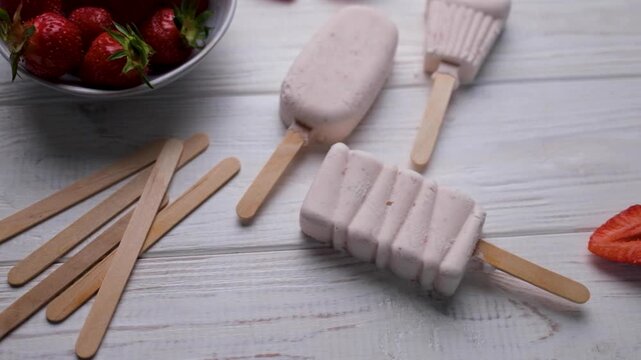 Homemade strawberry popsicles on a white wooden table