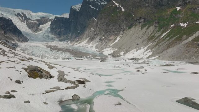 Low flying drone shot over glacier ice toward the twin glacier tongues of Austerdalsbreen in Norway with visible moraine, rugged ice textures, and blue skies.