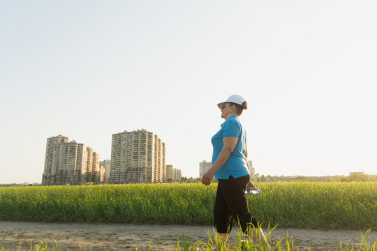 Active senior woman in sport clothes hiking on outdoor in the field with bottle of water. Summer season. Selective focus. Wellness, healthy lifestyle