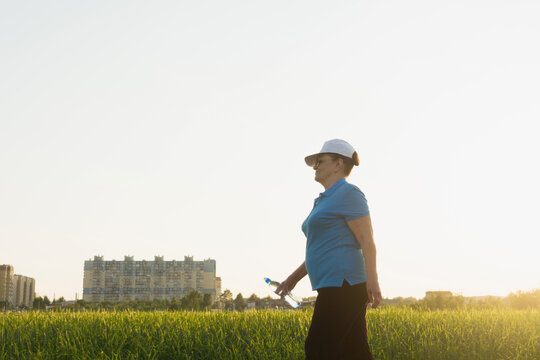 Active senior woman in sport clothes hiking on outdoor in the field with bottle of water. Summer season. Selective focus. Wellness, healthy lifestyle