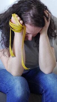 Sad woman obsessed with diet complaining sitting in couch at home and throwing measuring tape
