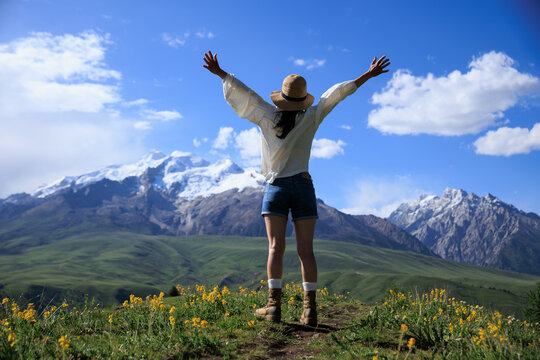 Woman open arms to snowcapped mountain on sunset grassland mountain top